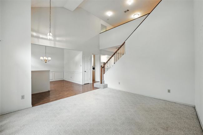 Unfurnished living room with carpet floors, a chandelier, high vaulted ceiling, stairs, and a wainscoted wall | Image 9