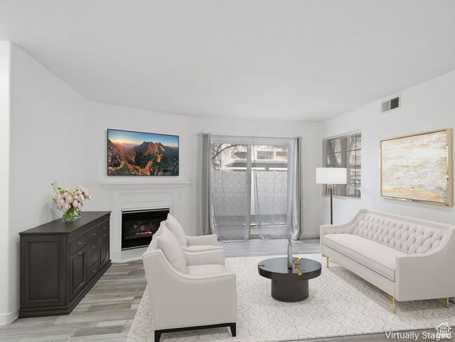 Living area with a glass covered fireplace, light wood-style flooring, visible vents, and baseboards | Image 5