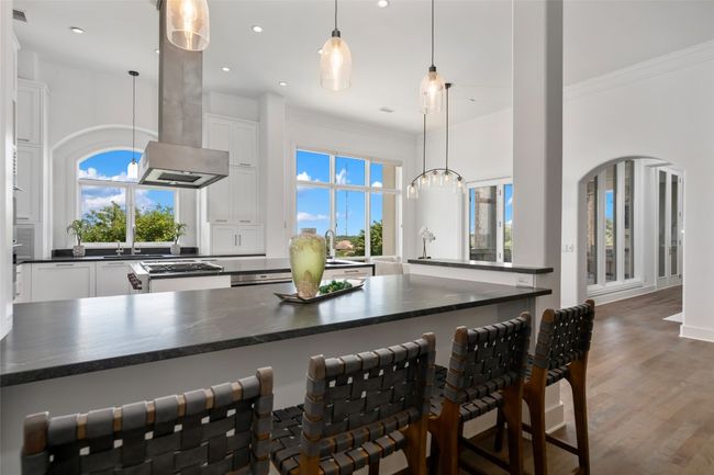 Kitchen featuring white cabinetry, island exhaust hood, crown molding, a kitchen bar, and wood finished floors | Image 12