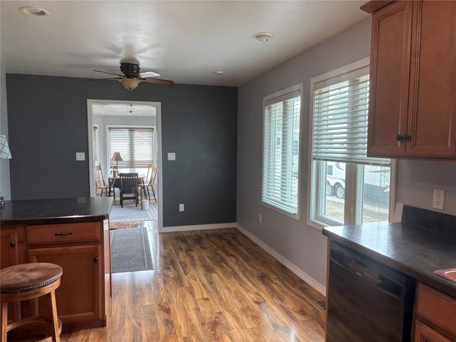 Kitchen with black dishwasher, dark countertops, ceiling fan, light wood finished floors, and baseboards | Image 8