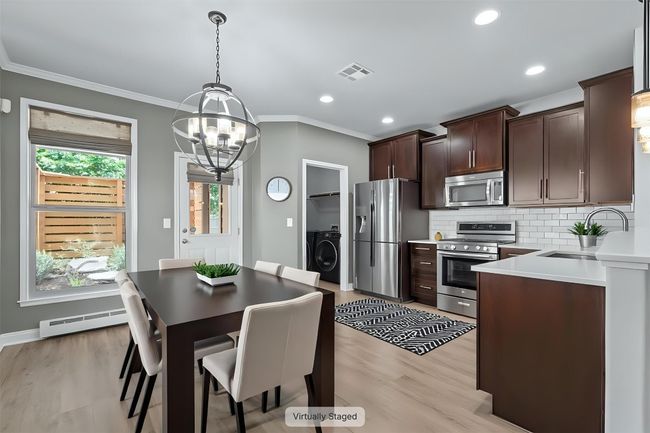 Kitchen with appliances with stainless steel finishes, a baseboard radiator, washer / dryer, a chandelier, and dark brown cabinetry | Image 4