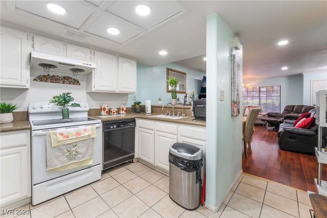 Kitchen featuring under cabinet range hood, black dishwasher, white cabinets, a sink, and white electric range | Image 13