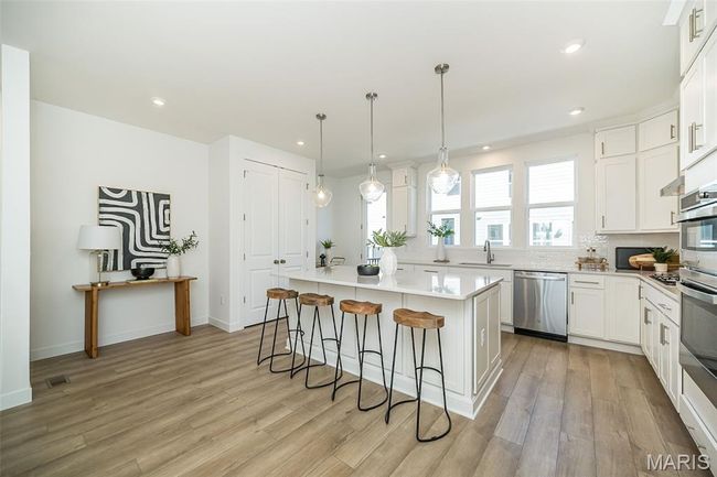 Kitchen featuring a breakfast bar area, a center island, light wood finished floors, light countertops, and white cabinets | Image 6