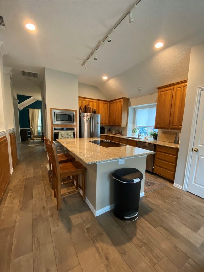 Kitchen featuring brown cabinetry, visible vents, rail lighting, vaulted ceiling, and stainless steel appliances | Image 15
