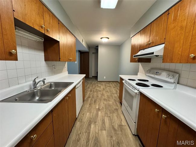 Kitchen with under cabinet range hood, white appliances, light wood-style flooring, backsplash, and light countertops | Image 15