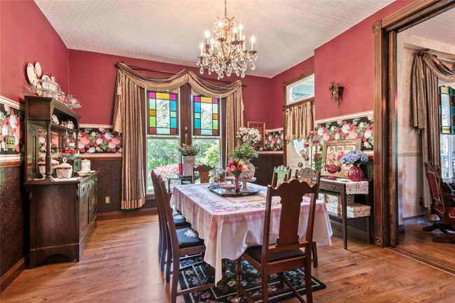 Dining area with a wainscoted wall, a textured ceiling, light wood-type flooring, a notable chandelier, and wallpapered walls | Image 7