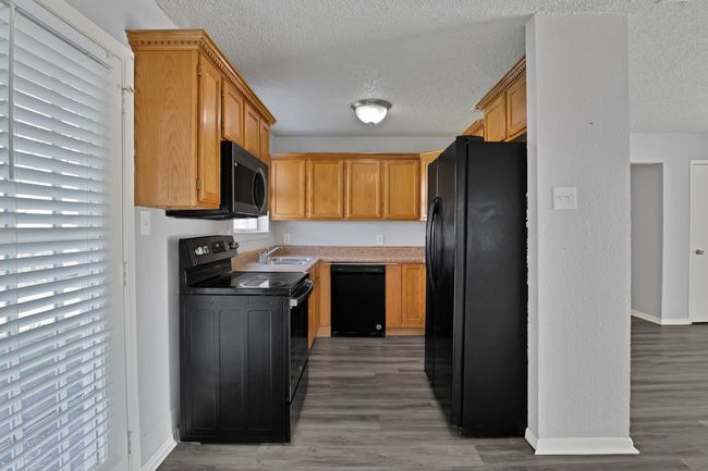 Kitchen featuring baseboards, light wood finished floors, a sink, black appliances, and a textured ceiling | Image 6