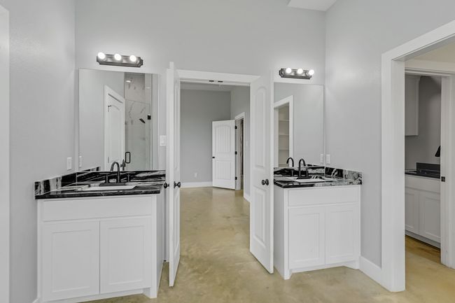 Full bathroom featuring a shower stall, two vanities, finished concrete flooring, and baseboards | Image 26