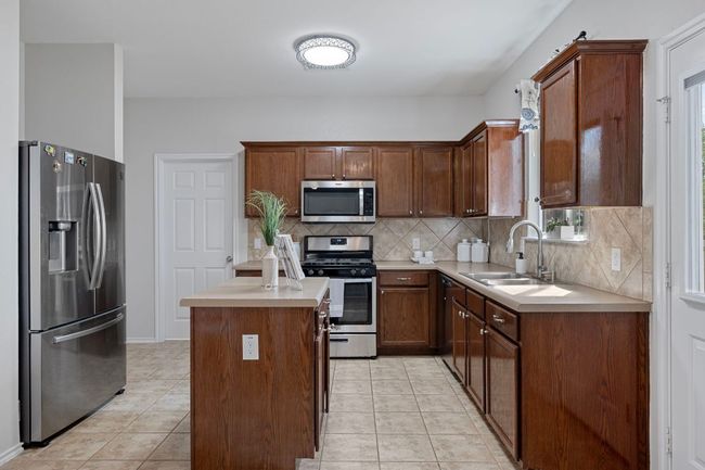 Kitchen with appliances with stainless steel finishes, a sink, backsplash, light countertops, and light tile patterned floors | Image 11