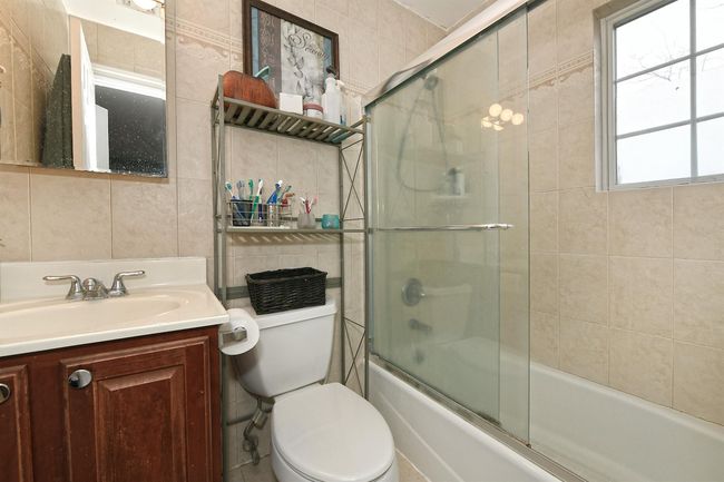 Full bathroom with vanity, toilet, tile walls, and bath / shower combo with glass door | Image 6