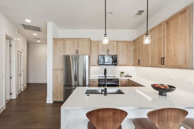 Kitchen featuring a peninsula, visible vents, light brown cabinetry, and appliances with stainless steel finishes | Image 8