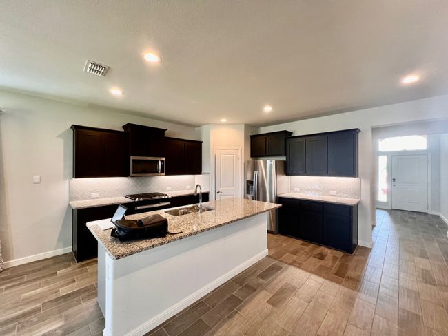 Kitchen with appliances with stainless steel finishes, light wood-style floors, backsplash, a center island with sink, and light stone counters | Image 4