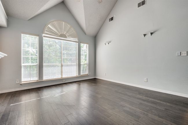 Unfurnished living room with vaulted ceiling, visible vents, and dark wood-style floors | Image 6