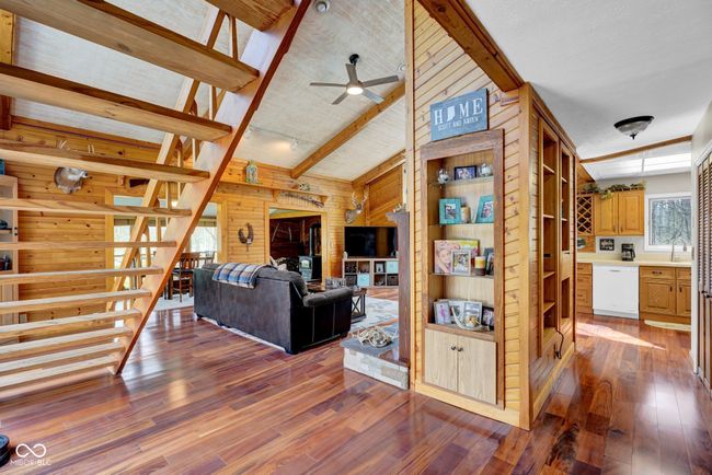 living area with brazilian cherry flooring, a ceiling fan, lofted ceiling with beams, and wood walls | Image 7