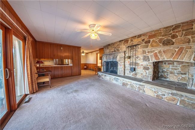 Unfurnished living room featuring a stone fireplace, carpet floors, ceiling fan, and wood walls | Image 11