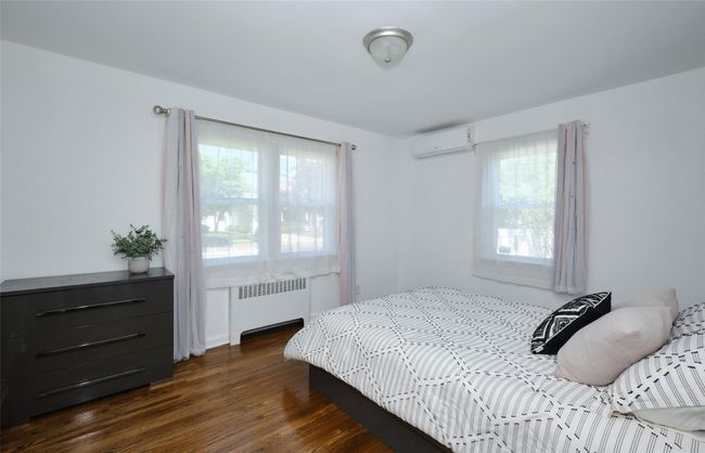 Bedroom with radiator heating unit, a wall mounted AC, and dark wood-style flooring | Image 15