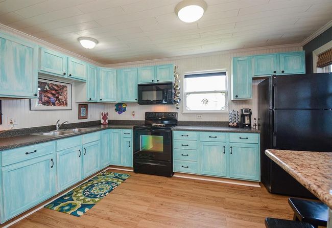 This kitchen features charming light blue cabinets, and black appliances.. It includes ample counter space, a double sink, and a window for natural light, creating a bright and inviting atmosphere. | Image 10