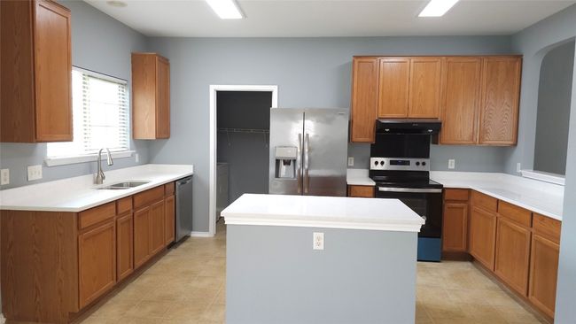 Kitchen with stainless steel appliances, exhaust hood, a kitchen island, light countertops, and arched walkways | Image 4