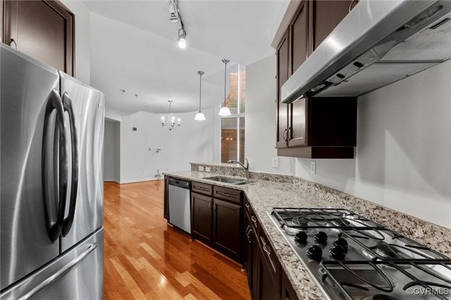 Kitchen featuring under cabinet range hood, stainless steel appliances, dark brown cabinets, a sink, and a notable chandelier | Image 11