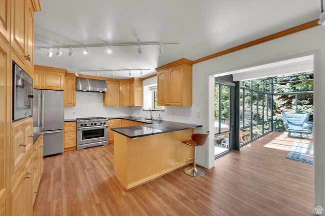 Kitchen featuring premium appliances, wall chimney range hood, a peninsula, track lighting, and light wood finished floors | Image 7