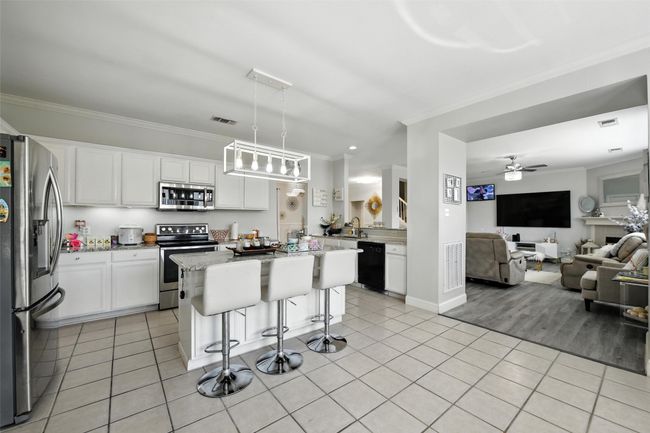 Kitchen featuring appliances with stainless steel finishes, ornamental molding, open floor plan, light tile patterned floors, and white cabinetry | Image 14