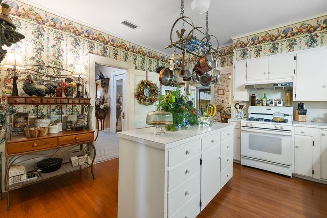 Kitchen with white range with gas stovetop, under cabinet range hood, light countertops, dark wood-style floors, and wallpapered walls | Image 13