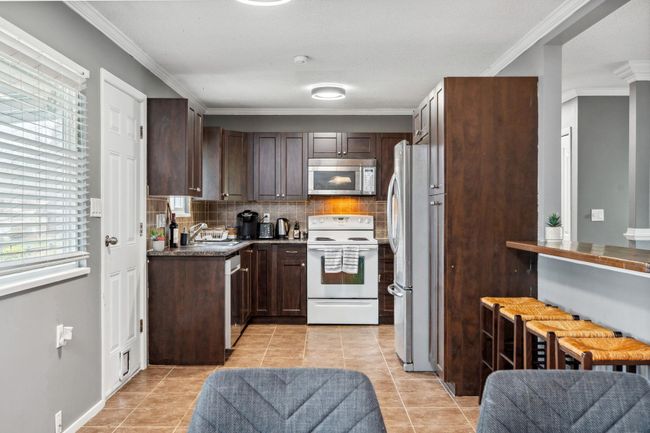 Kitchen featuring stainless steel appliances, dark brown cabinetry, a sink, and decorative backsplash | Image 12