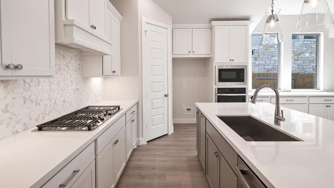 Kitchen featuring wood finished floors, stainless steel appliances, white cabinetry, backsplash, and decorative light fixtures | Image 15