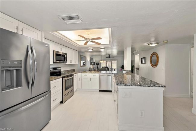 Kitchen featuring appliances with stainless steel finishes, a peninsula, a tray ceiling, white cabinetry, and dark stone counters | Image 7