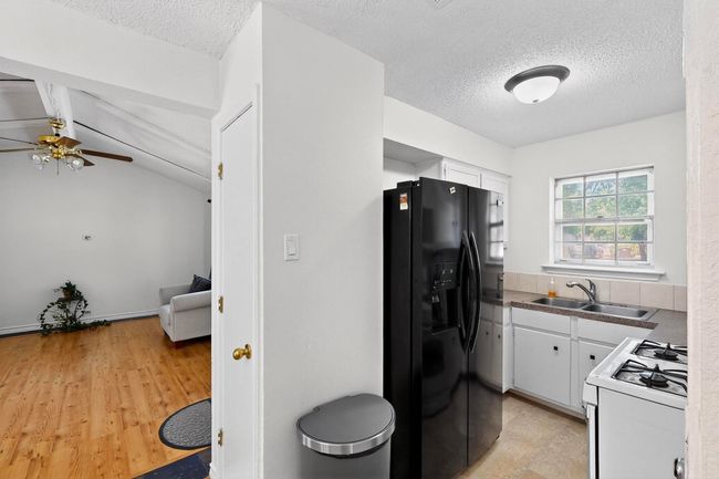 Kitchen featuring white gas stove, black refrigerator with ice dispenser, white cabinetry, a ceiling fan, and a textured ceiling | Image 6