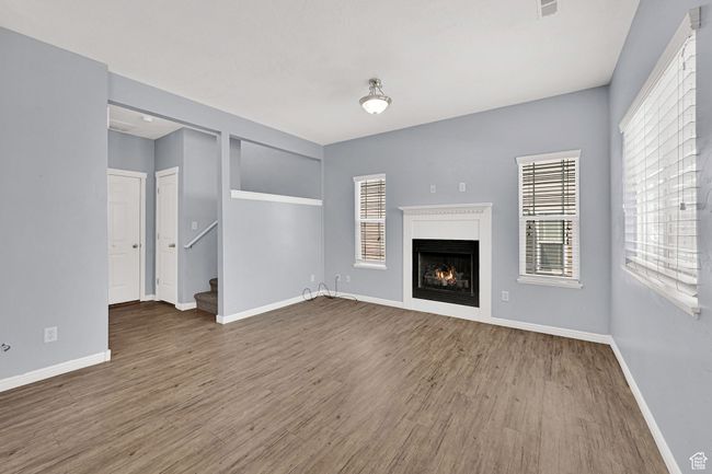 Unfurnished living room with wood finished floors, a lit fireplace, and stairway | Image 11