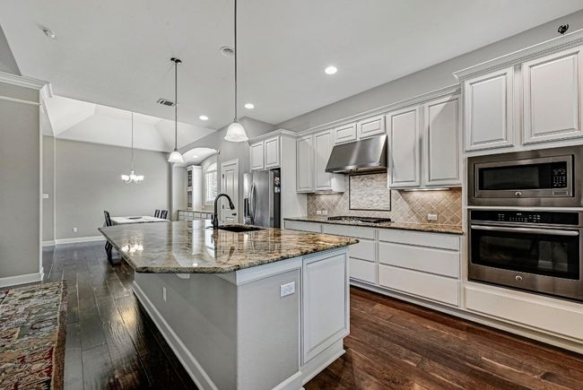 Kitchen with appliances with stainless steel finishes, under cabinet range hood, an island with sink, dark wood-style flooring, and tasteful backsplash | Image 11