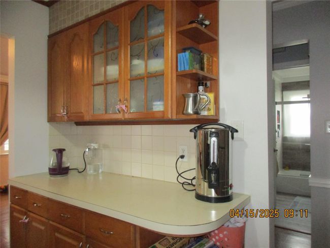Kitchen with glass insert cabinets, brown cabinets, light countertops, and decorative backsplash | Image 5