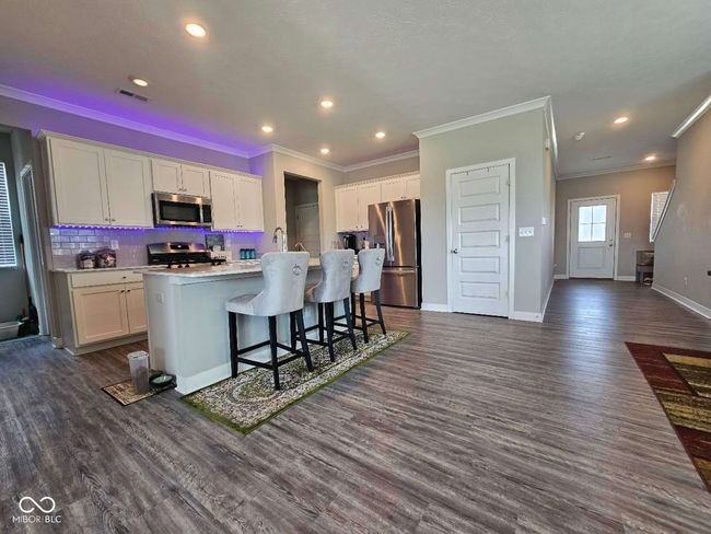 kitchen with stainless steel appliances, ornamental molding, white cabinets, a center island with sink, and dark wood-style floors | Image 9