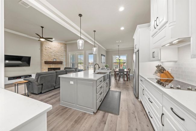 Kitchen with tasteful backsplash, visible vents, black electric cooktop, ornamental molding, and freestanding refrigerator | Image 7
