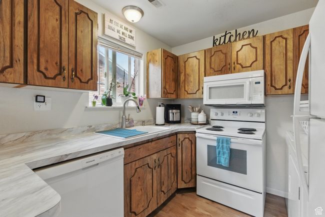 Kitchen featuring brown cabinetry, light countertops, white appliances, and a sink | Image 27