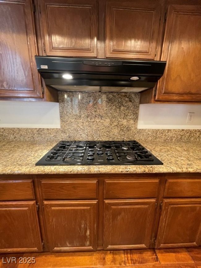 Kitchen featuring cooktop, range hood, decorative backsplash, and brown cabinetry | Image 8