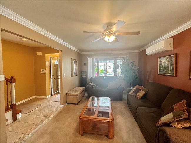 Tiled living room with ceiling fan, crown molding, and an AC wall unit | Image 5