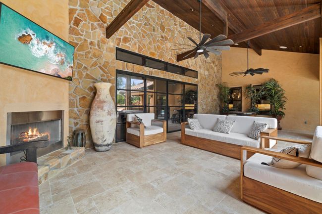Patio with stone wall, gas outdoor fireplace, wood vaulted ceilings, travertine tile, double iron doors leading into living room. | Image 4