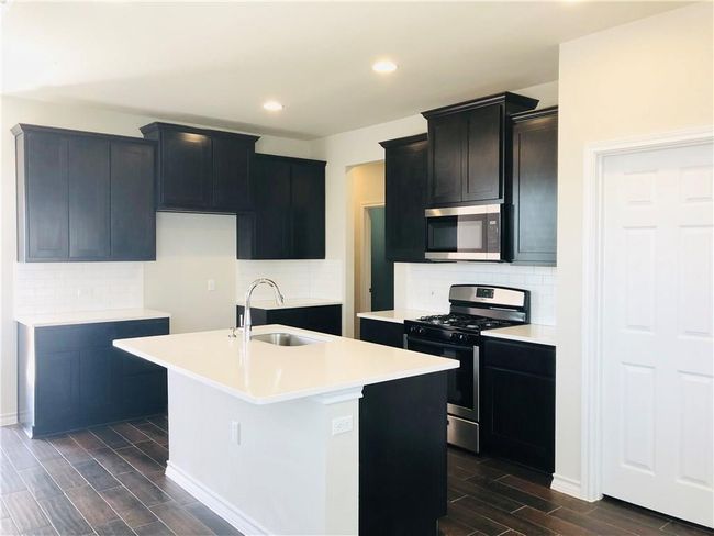 Kitchen featuring stainless steel appliances, wood tiled floors, tasteful backsplash, a center island with sink, and recessed lighting | Image 5