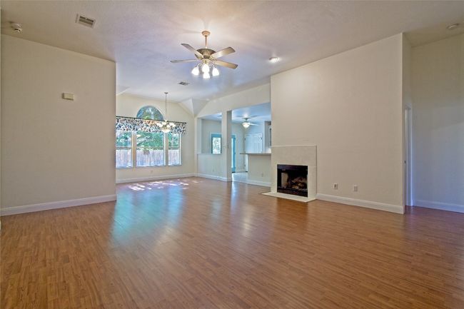 Unfurnished living room with a ceiling fan, wood finished floors, lofted ceiling, and a fireplace | Image 6