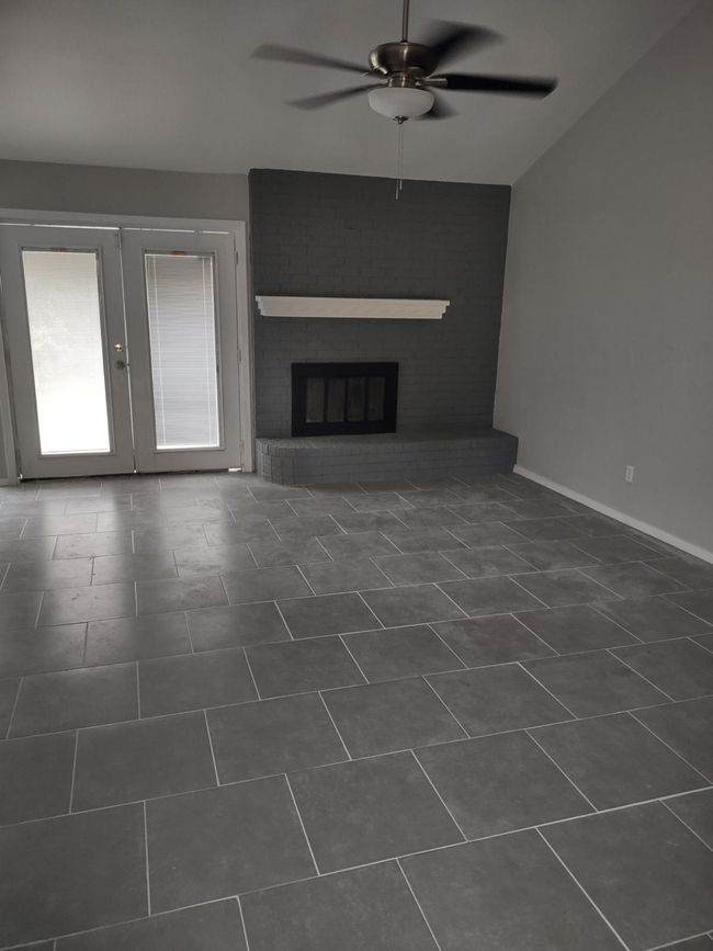 Unfurnished living room featuring a ceiling fan, french doors, a fireplace, and dark tile patterned flooring | Image 12