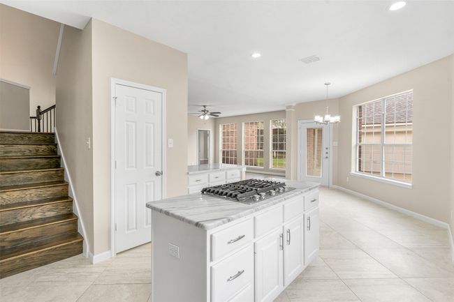 Kitchen featuring white cabinets, stainless steel gas cooktop, recessed lighting, a kitchen island, and decorative light fixtures | Image 14