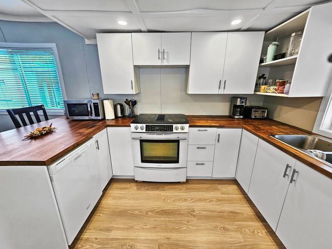 Kitchen with dishwasher, electric stove, butcher block counters, stainless steel microwave, and open shelves | Image 4