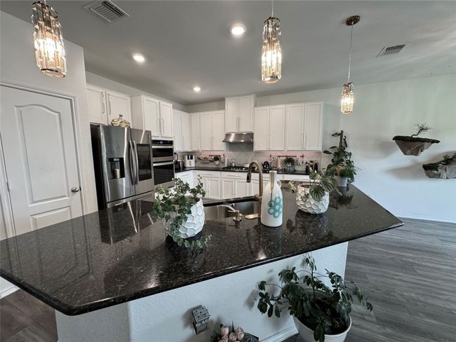 Kitchen with appliances with stainless steel finishes, a chandelier, under cabinet range hood, white cabinetry, and tasteful backsplash | Image 10