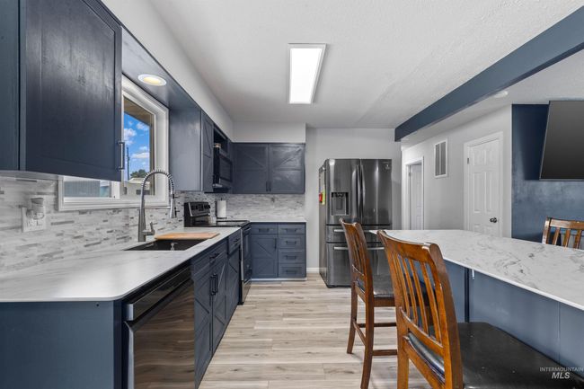 Kitchen featuring stainless steel fridge, range with electric cooktop, black dishwasher, light wood-style flooring, and tasteful backsplash | Image 14