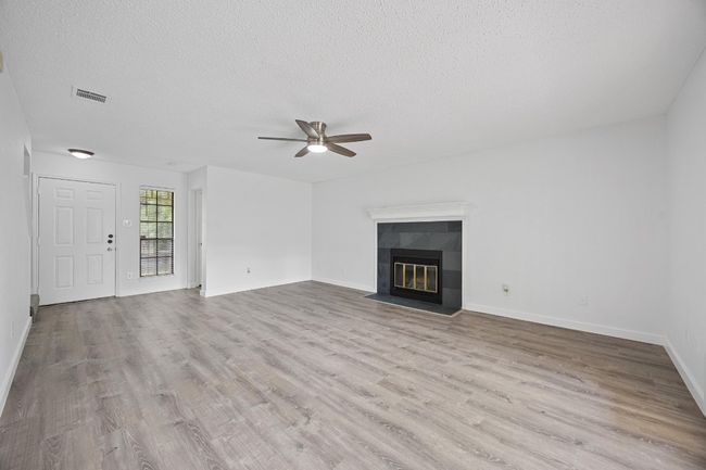 Unfurnished living room with a ceiling fan, wood finished floors, a textured ceiling, a tile fireplace, and visible vents | Image 7