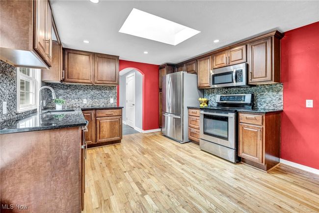 Kitchen featuring appliances with stainless steel finishes, a skylight, radiator heating unit, light wood flooring, and maple cabinetry | Image 7