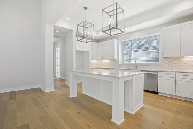 Kitchen featuring an inviting chandelier, light wood-style flooring, white cabinetry, dishwasher, and light countertops | Image 15
