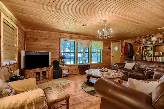 Living room with a notable chandelier, wooden walls, wood finished floors, and wood ceiling | Image 16